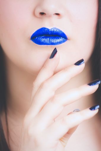 A vertical closeup shot of a female wearing blue and white lipstick with a black manicure - great for an article about cosmetics