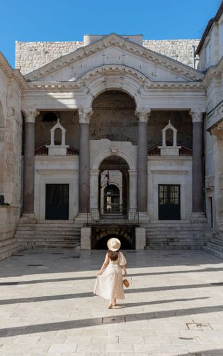 A back shot of a young woman standing on the floor at the peristyle of the amazing Diocletian's palace on a sunny day in Split, Croatia
