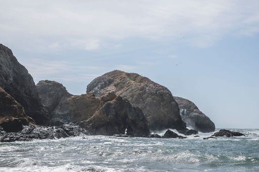 A beautiful landscape view of sea waves crashing on rock formations at the beach against cloudy sky on a sunny day