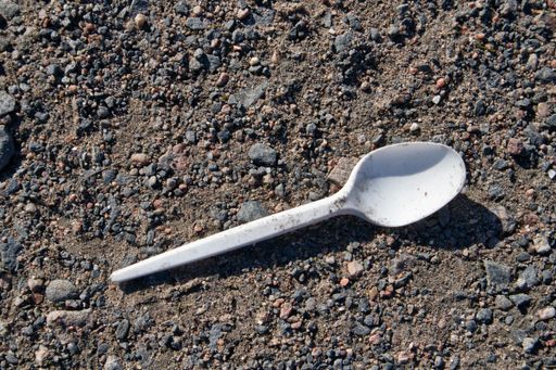 A closeup shot of an abandoned plastic white spoon on gravel