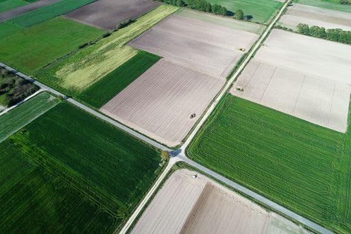 Aerial view from the drone, a bird's eye view of agricultural fields with a road through and a tractor on it in the spring