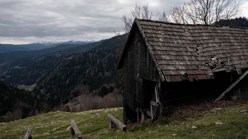 The old abandoned rustic hut against the background of hills and cloudy sky.