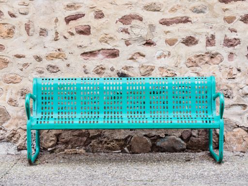 A green metal bench in front of a stone wall at daytime