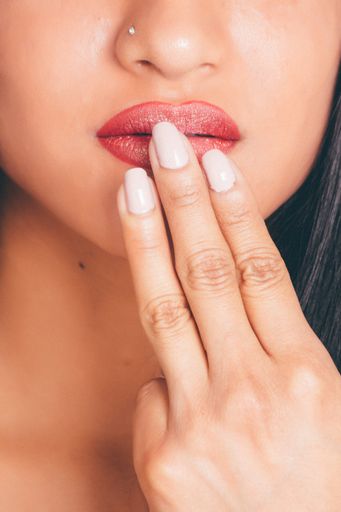 A closeup shot of a female wearing a red lipgloss touching her lips- great for an article about cosmetics