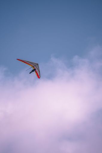 A vertical shot of a hang glider with red line in the blue sky with a beautiful cloud
