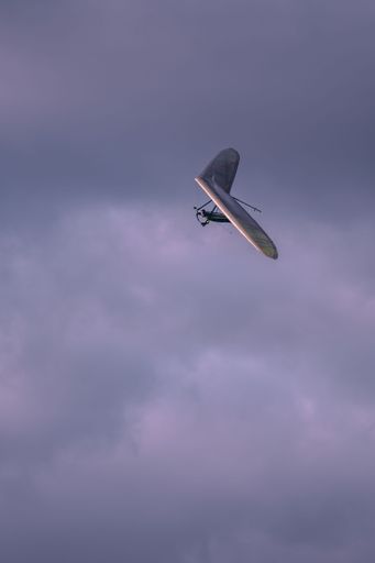 A vertical shot of a hang glider flying in the gloomy gray sky
