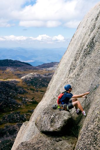 A vertical shot of a young male climbing a mountain with special equipment on a sunny day