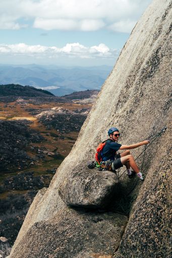 A vertical shot of a young male climbing a mountain with special equipment on a sunny day