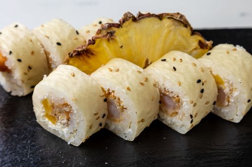 Eight pieces of sushi rolls with pineapple on a black wooden board