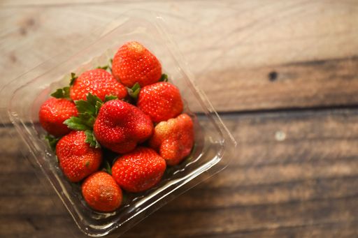 A top view of red juicy strawberries in a plastic plate on a wooden table