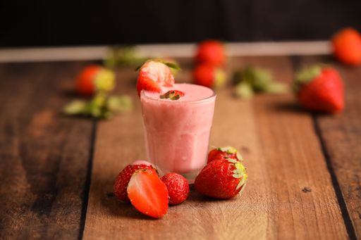 A closeup shot of a pink strawberry smoothie in a glass cup on a wooden table
