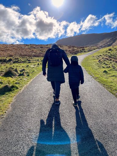 A vertical shot of a father and a son walking on the road in the mountains