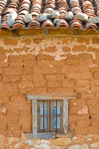 A vertical shot of an old adobe wall and a small window in Castile, Spain