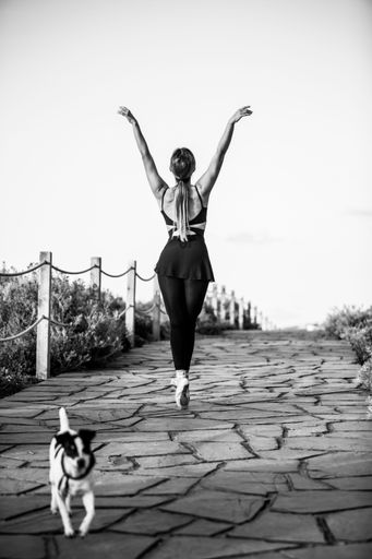 A vertical shot of a ballerina with a neat figure and the Jack Russell terrier in grayscale
