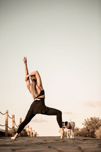 A vertical shot of a ballerina in a flexible pose and the Jack Russell terrier at the sunset
