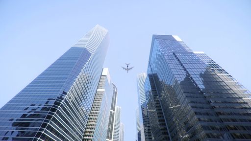 A Low angle shot of an airplane flying above modern skyscrapers in city center