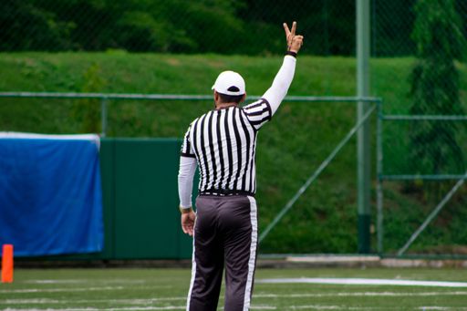 A back shot of a Male referee doing a fist sign during a Flag football match in the green field