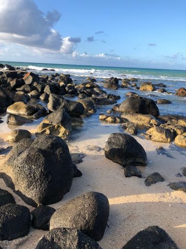 A vertical shot of big rocks on a sandy beach with the calm waves in the background