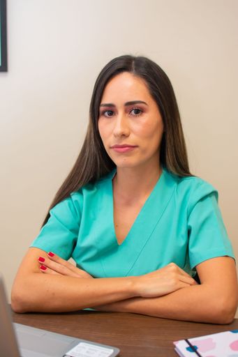A young female nurse in green uniform with her arms crossed sitting in front of the desk