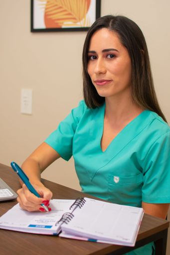 A vertical shot of young female nurse in green uniform taking notes in the notebook on her desk