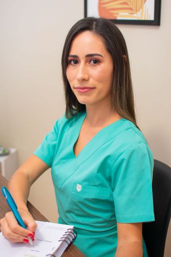 A vertical shot of young female nurse in green uniform taking notes in the notebook on her desk