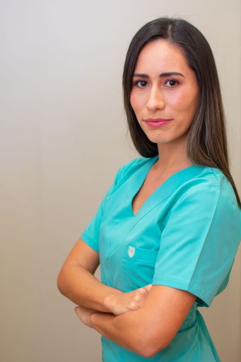 A vertical shot of young female nurse in green uniform with her arms crossed standing against gray wall