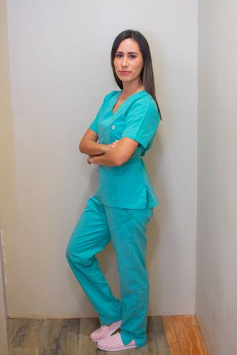 A young female nurse in green uniform with her arms crossed standing against gray wall