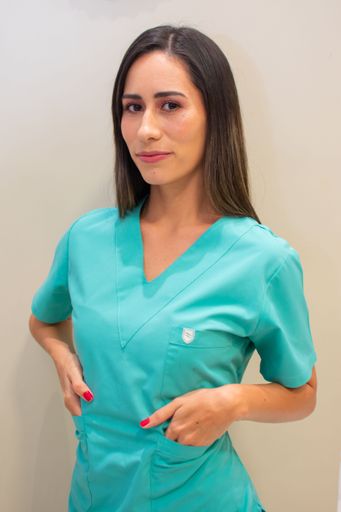 A young female nurse in green uniform with her hands in the pockets standing against gray wall
