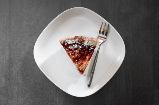 A high angle shot of a piece of a delicious strawberry pie in a white ceramic plate beside a fork