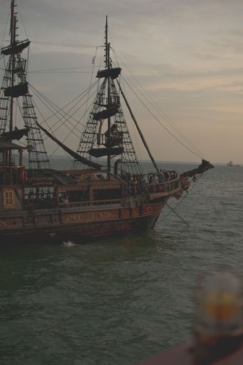 A vertical shot of a pirate ship sailing in a sea at sunset