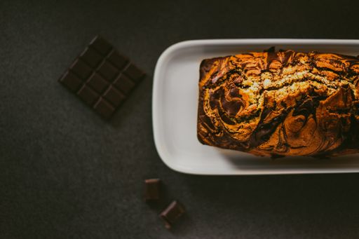 A high angle shot of a chocolate cake in a white plate beside chocolate bars on a wooden surface