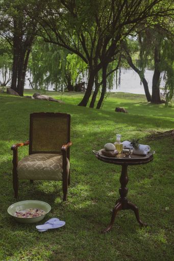 The rose petals with essential oils in a tub next to white flippers, armchair, and table in the garden