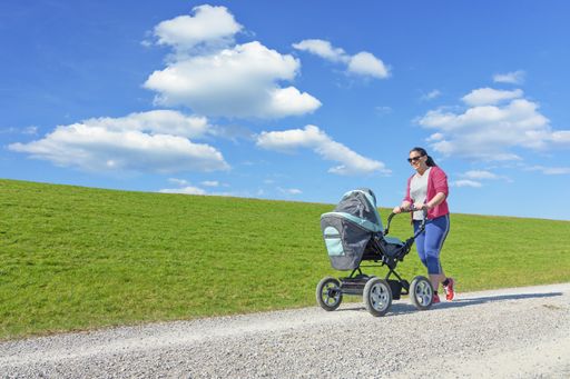 A young female in sportswear walking with a baby carriage in a field under the sunlight