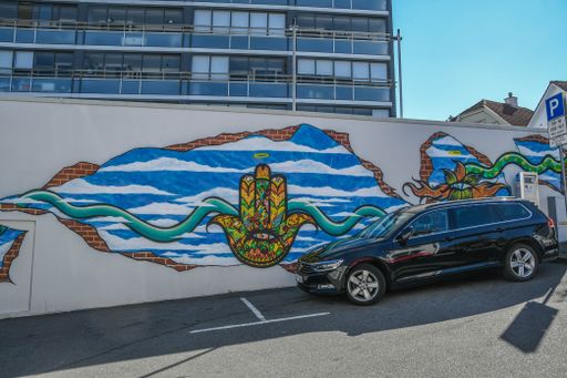 A graffiti modern art design on a wall with a black car in front of it