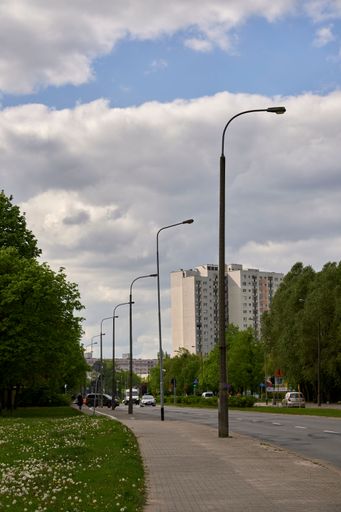 A vertical shot of a row of high lamps by a sidewalk and street with an apartment building