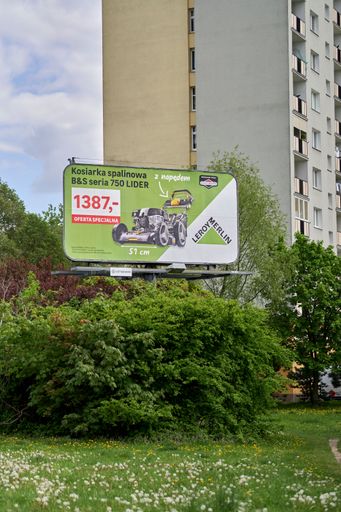 A vertical shot of the Leroy Merlin billboard by an apartment building above the beautiful greenery