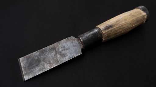 A closeup shot of an old rusty chisel with wooden handle isolated on a black background