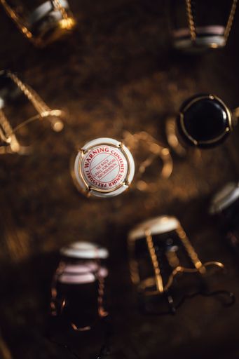 Warning: contents under pressure, champagne cage on brass tray with many other cages, drinking too much, excess
