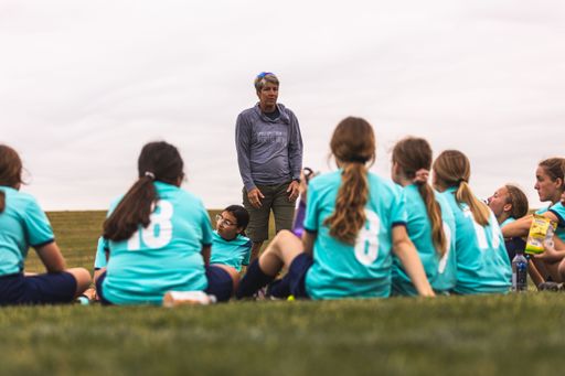 A group of young girls in blue uniforms and the coach having a discussion during the break at Youth Soccer Game