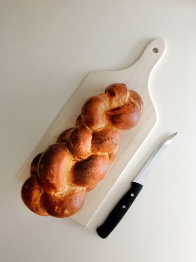 A vertical high angle shot of challah on a white chopping board beside a knife on a white surface