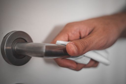 A closeup shot of a human hand cleaning a door handle with a wet wipe