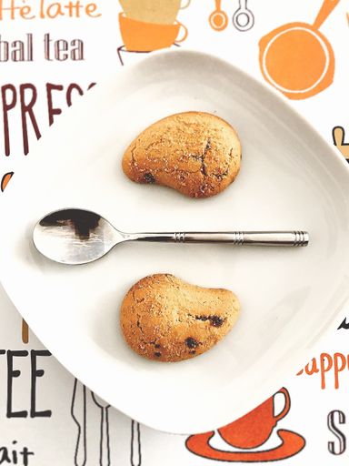 A vertical high angle shot of two cookies and a silver spoon in a white plate on the table