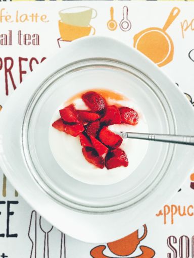 A vertical high angle shot of tasty yogurt with chopped strawberries on top beside a silver spoon on a black surface