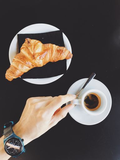 A high angle shot of a warm cup of coffee and a delicious croissant on the side