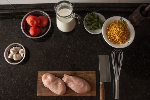 A top view of chicken breast, milk, corn and other ingredients on the kitchen table