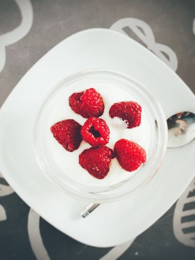 A vertical high angle shot of tasty yogurt with red berries on top beside a silver spoon on a black surface