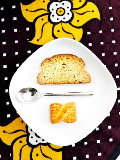 A vertical high angle shot of a silver spoon between a slice of bread and a cookie in a white plate
