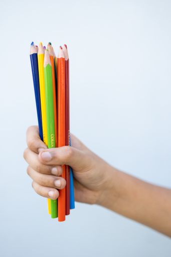 A child holding colorful drawing pencils on a white background