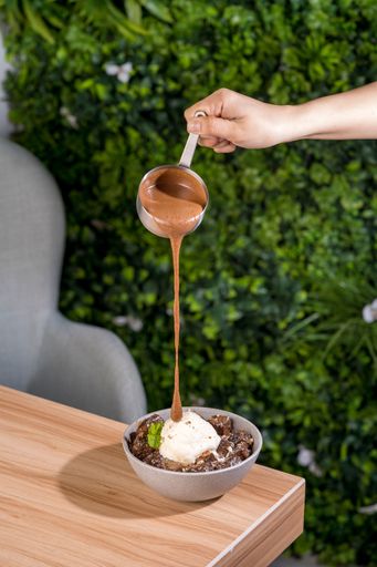 A selective of a hand pouring chocolate on a bowl of ice cream