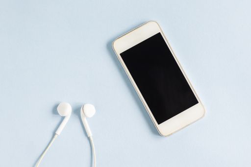 A closeup shot of a white smartphone and earphones on a light blue background